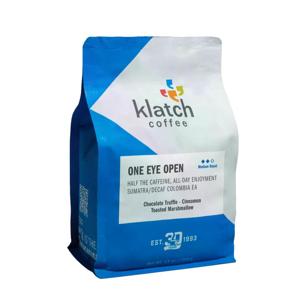 A 12 oz bag of Klatch Coffee 'One Eye Open' medium roast coffee, featuring a blue and white geometric design with a multicolor logo on a white background. – Klatch Coffee main product