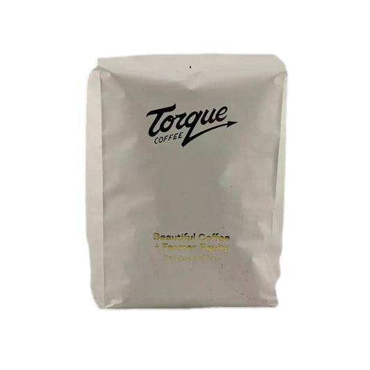 A box of Torque Coffee Bombón candy-coated lollipops, featuring a white box with gold script lettering and a bright pink side panel. product