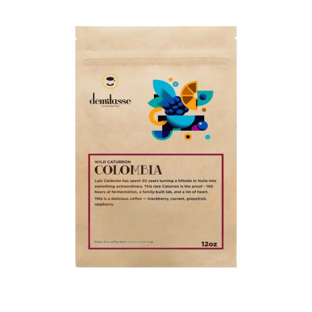 A 12oz stand-up kraft paper pouch of Demlassse Wild Caturron Colombia coffee, featuring a colorful graphic illustration of coffee beans, citrus, and leaves on a white background. – Demitasse main product