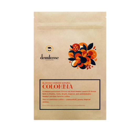A stand-up kraft paper coffee bag from demlasse, featuring a colorful floral graphic in orange, black, and red, and a label for 'El Diviso Chigroso Natural Colombia' on a white background.