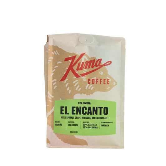 A stand-up coffee bag from Kuma Coffee, featuring a cream-colored design with a large red script logo and a bright green label that reads 'EL ENCANTO'.