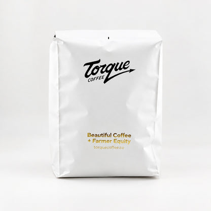 A white bag of Torque Coffee on a clean white background, featuring the black Torque Coffee logo and gold text reading 'Beautiful Coffee + Farmer Equity' with the website below.