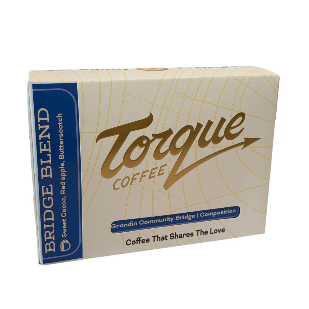 A box of Torque Coffee Bridge Blend coffee, featuring a cream-colored box with gold grid lines, a blue vertical banner on the left, and gold and blue branding. – Torque Coffees main product